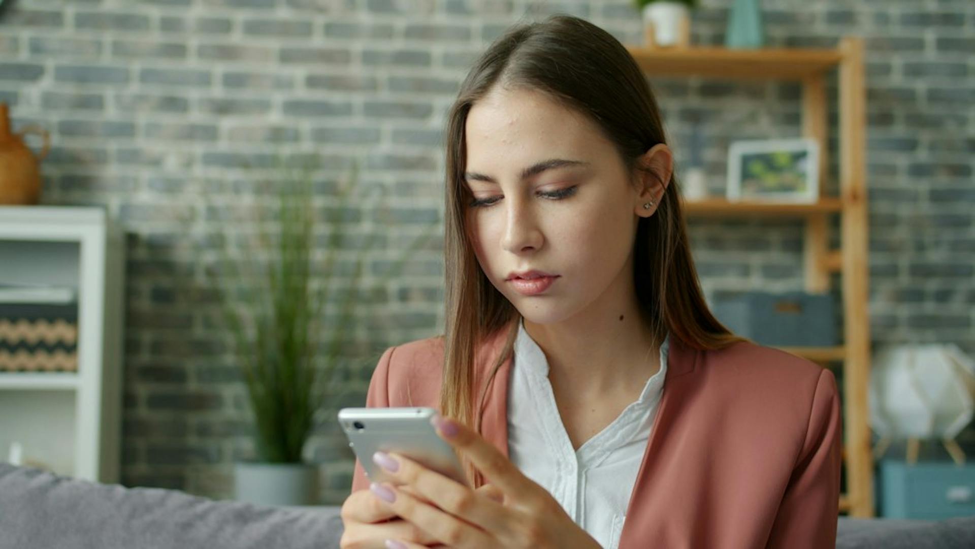 Young woman reading a notification on her smartphone at home (Photo by Vitaly Gariev on Unsplash)