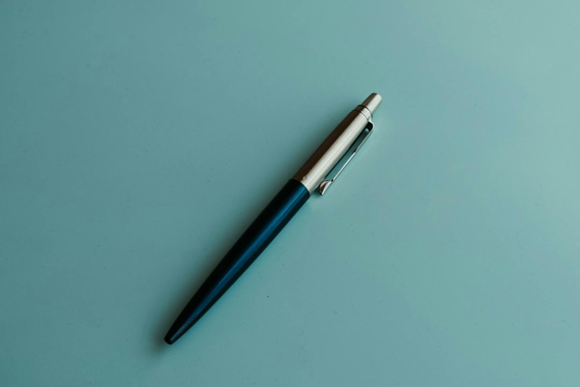 Dark blue ballpoint pen on a turquoise background (Photo by Liviu C. on Unsplash)
