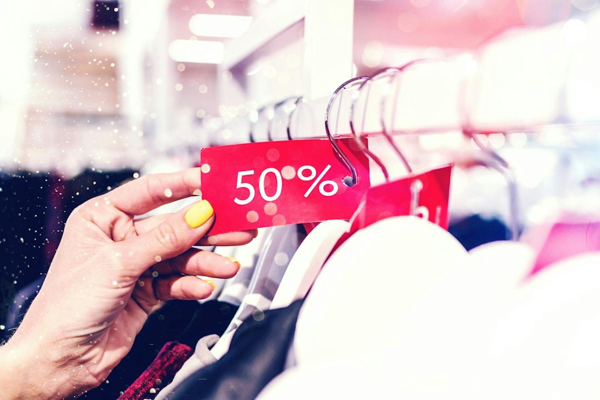 Hand hält ein rotes Rabattschild mit 50 Prozent in einem Modegeschäft (Photo by Artem Beliaikin on Unsplash)
