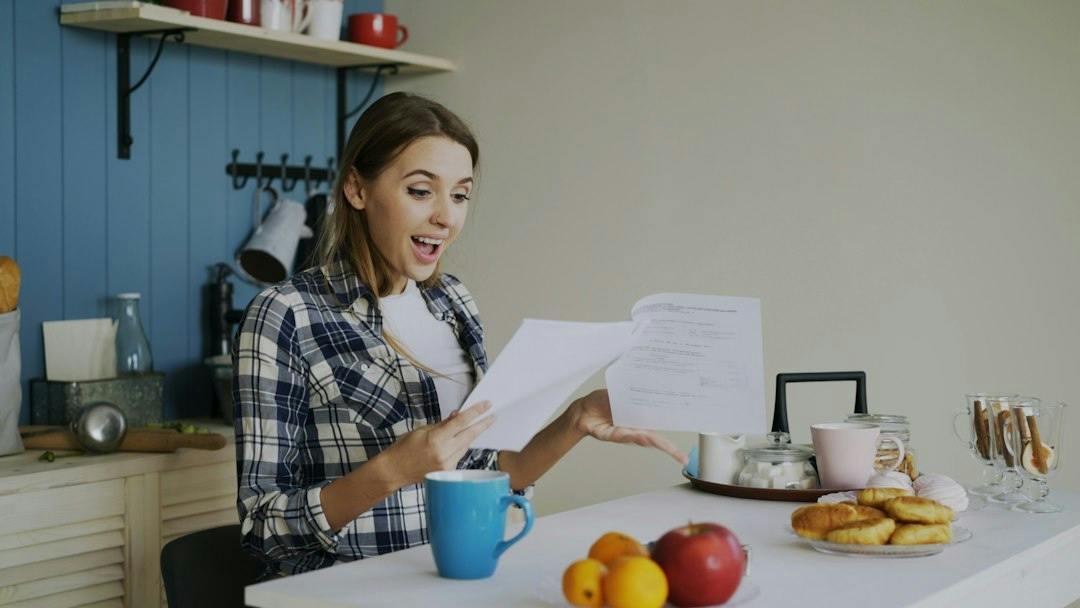 Junge Frau liest Unterlagen am Küchentisch mit einer Tasse (Photo by Vitaly Gariev on Unsplash)