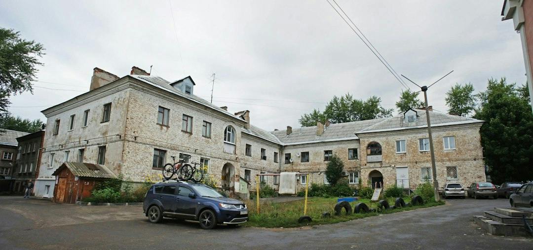 Old residential building with a car parked in the courtyard on a grey day (Photo by Boris Busorgin on Unsplash)
