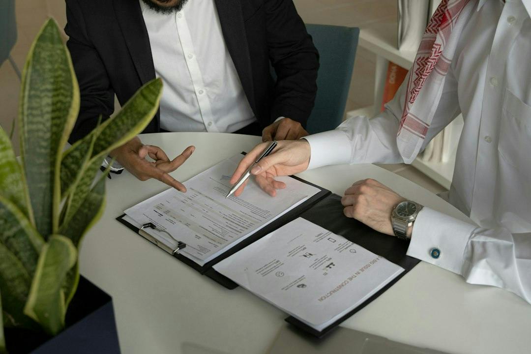 Two people going through a document on a clipboard at a meeting table (Photo by Amina Atar on Unsplash)