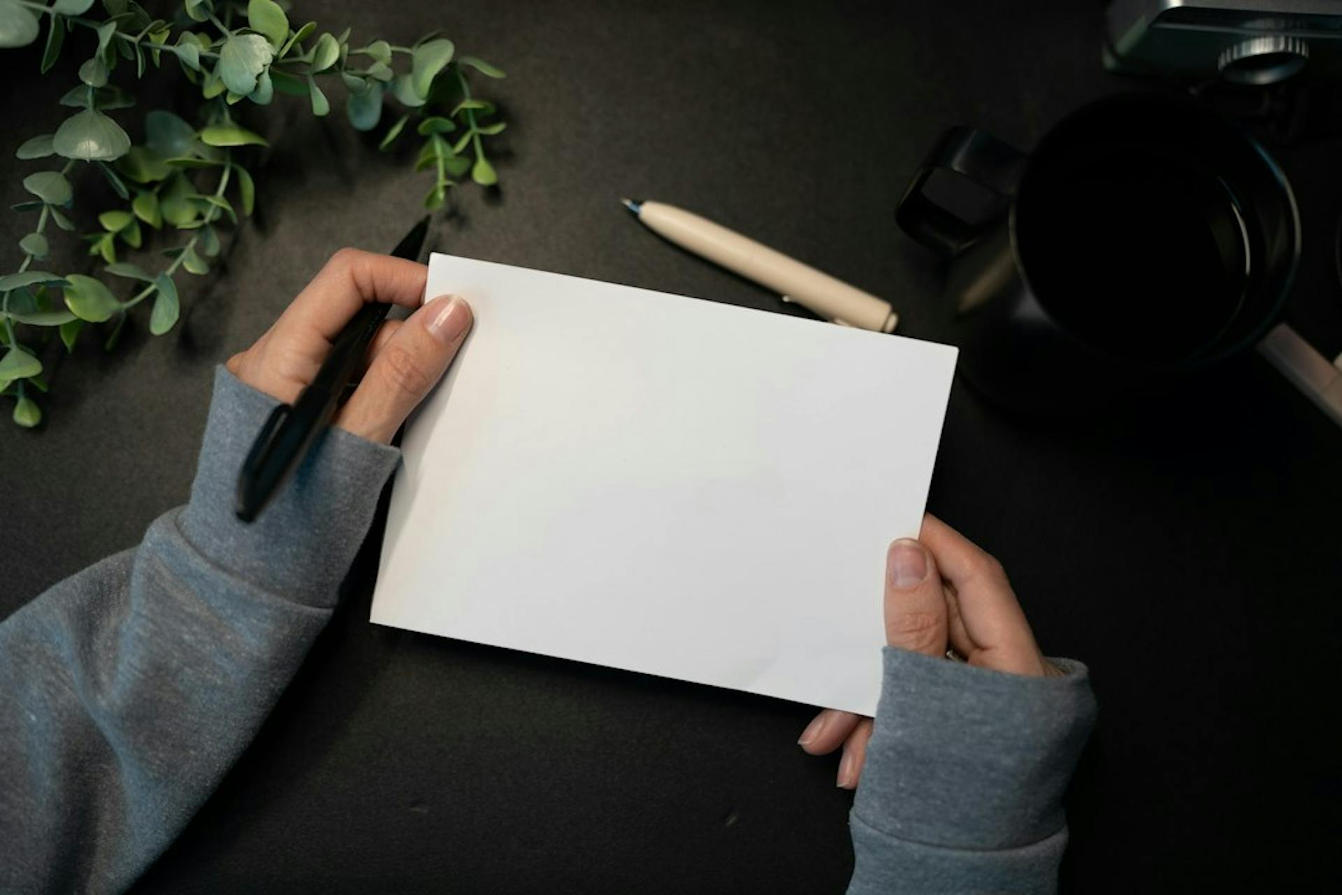 Person holding a blank sheet of paper and a pen at a dark desk (Photo by Kelly Sikkema on Unsplash)