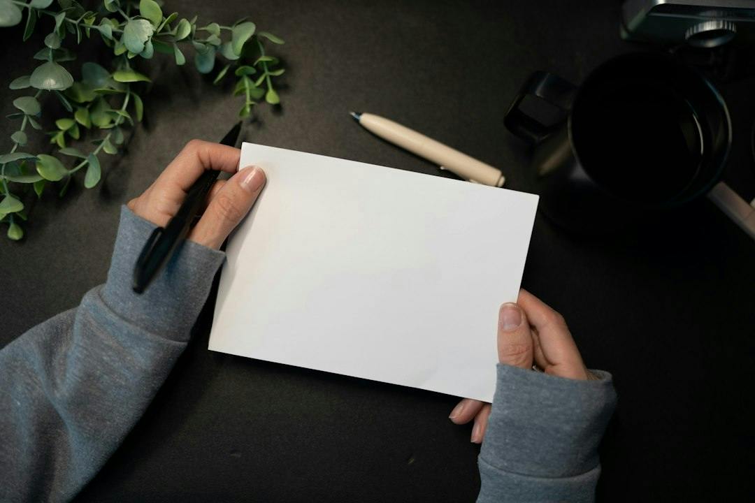 Person holding a blank sheet of paper and a pen at a dark desk (Photo by Kelly Sikkema on Unsplash)
