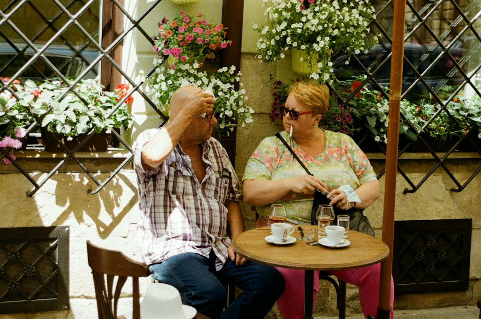 Older couple drinking coffee at a café table among flowers (Photo by Maryna Nikolaieva on Unsplash)