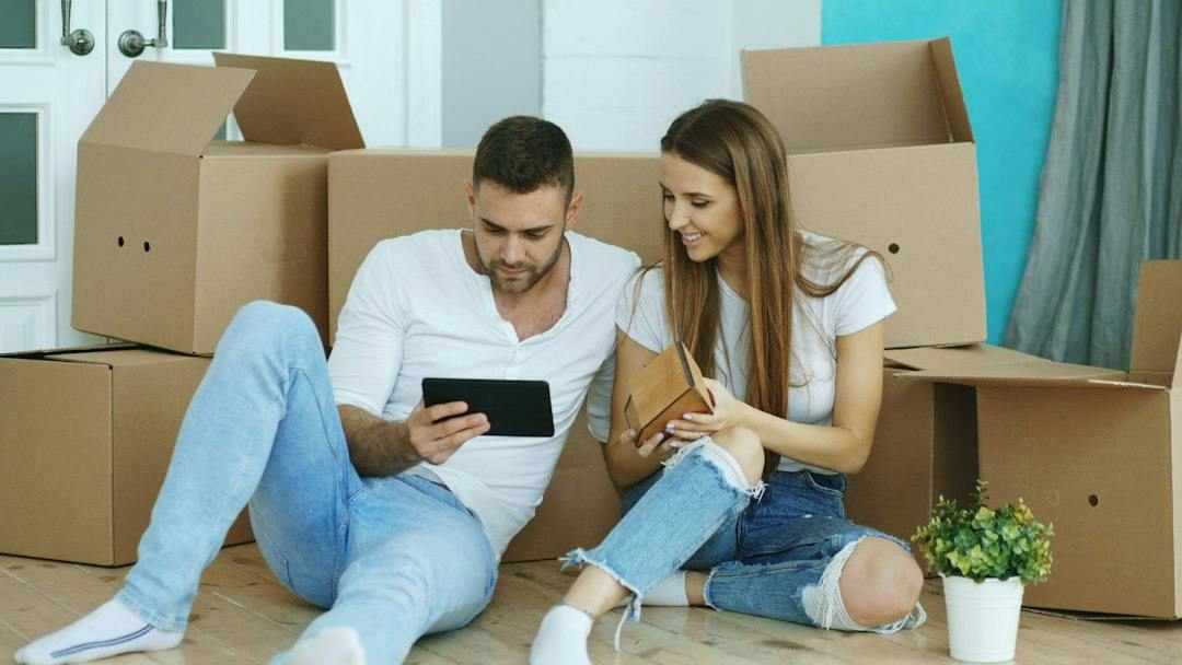 Young couple sitting among moving boxes with a tablet (Photo by Vitaly Gariev on Unsplash)