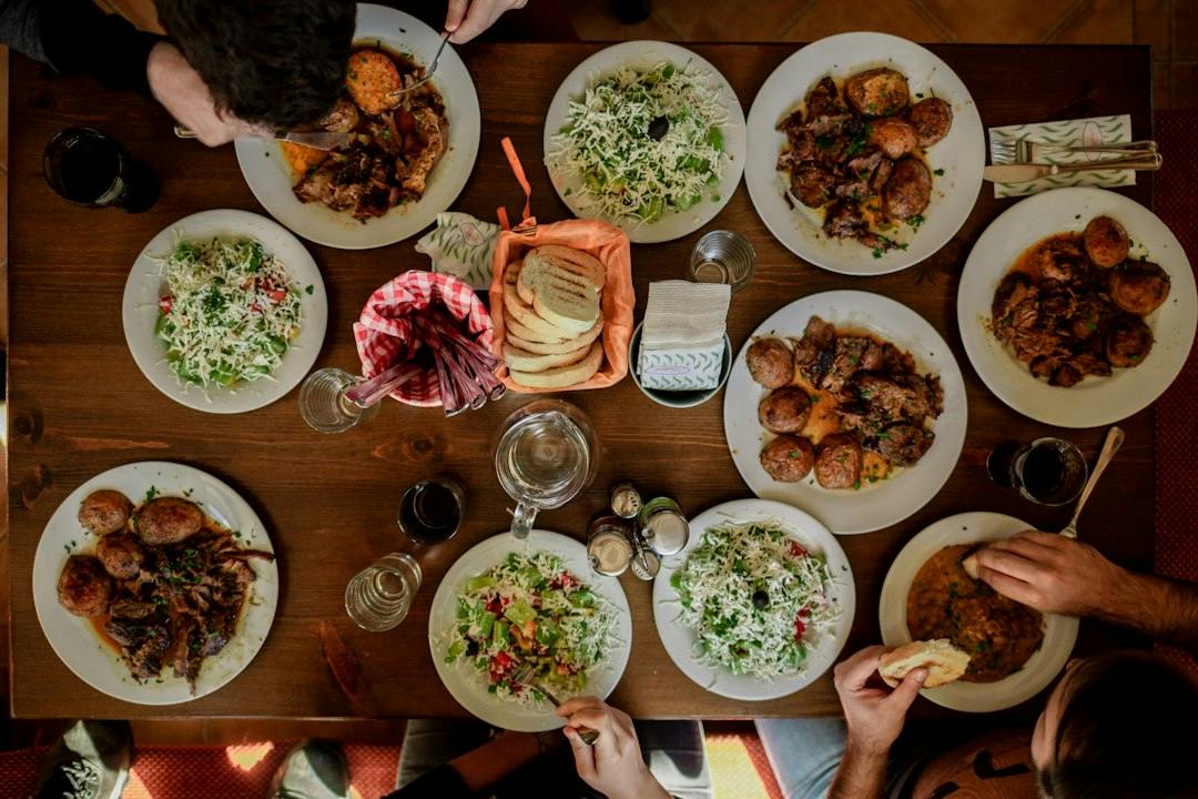 Many plates of food shared on a long table seen from above (Photo by Stefan Vladimirov on Unsplash)