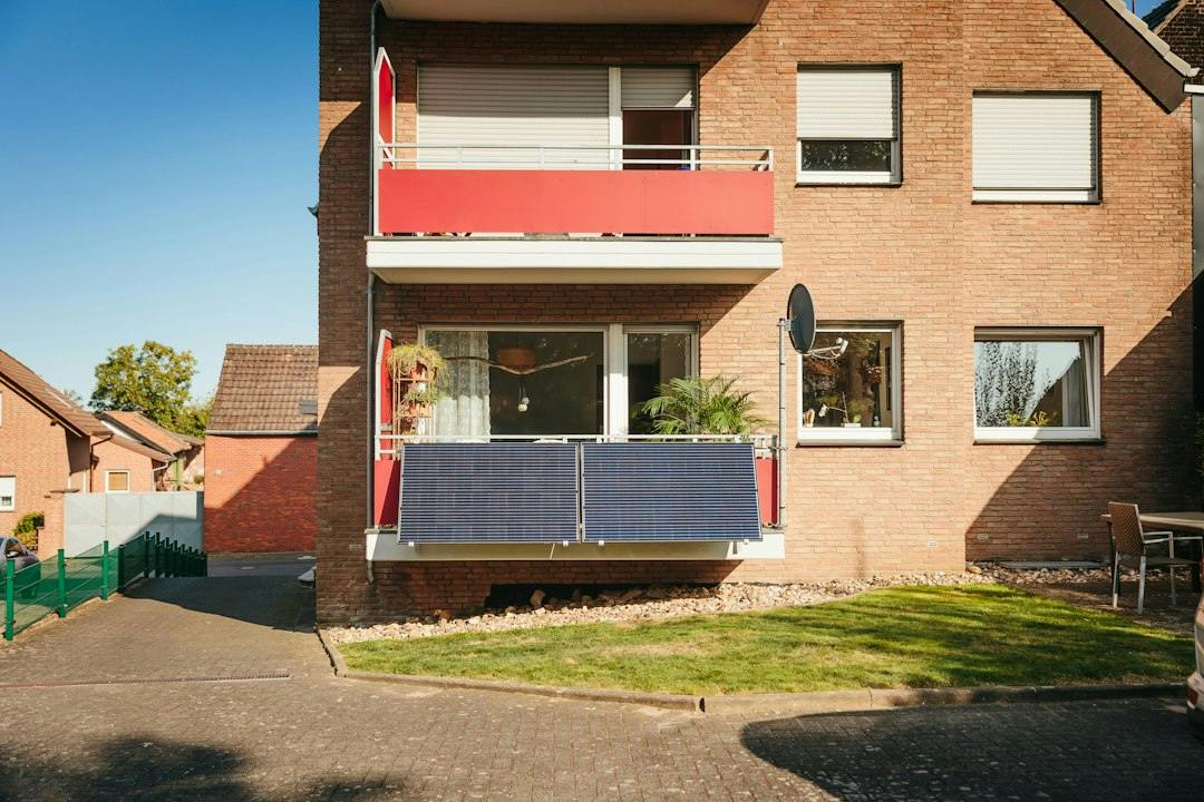 Brick apartment building with a balcony fitted with solar panels (Photo by Yuma Solar on Unsplash)