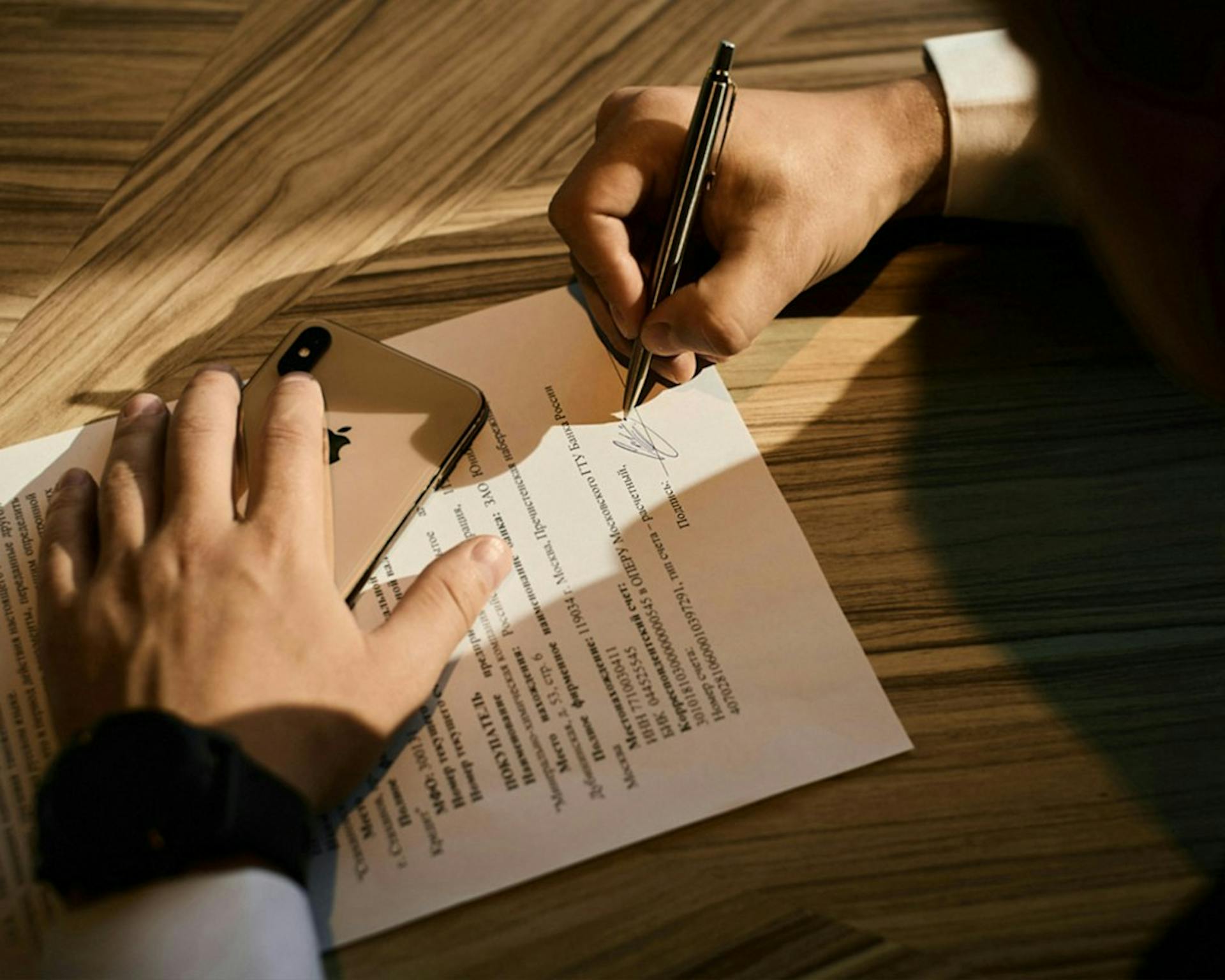 Person underskriver en kontrakt på et træbord (Photo by Signature Pro on Unsplash)