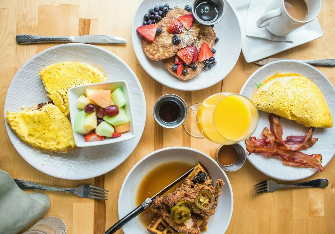 Morgenmadstallerkener med omelet, frugt og kaffe på et fælles bord (Photo by Heather Ford on Unsplash)