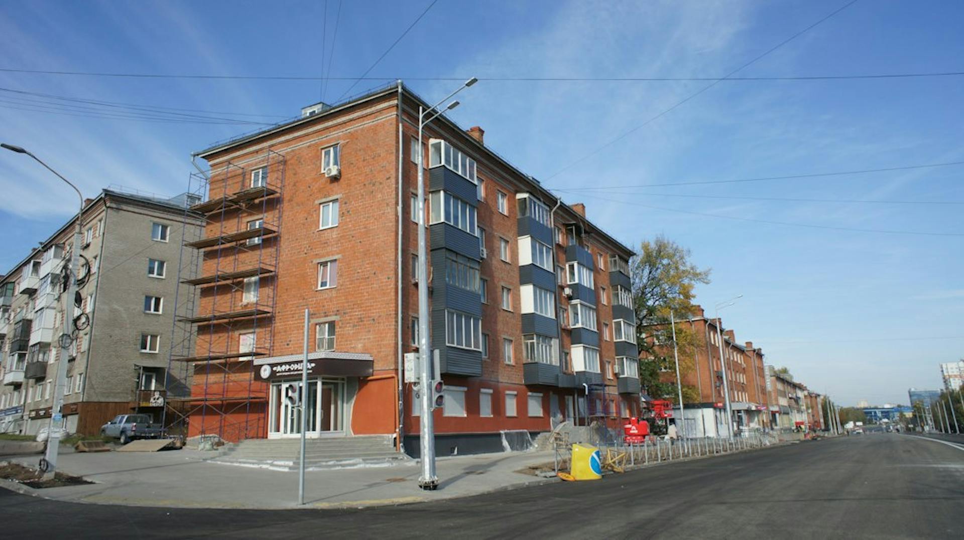 Rød murstensboligblok ved en bred gade under en blå himmel (Photo by Boris Busorgin on Unsplash)