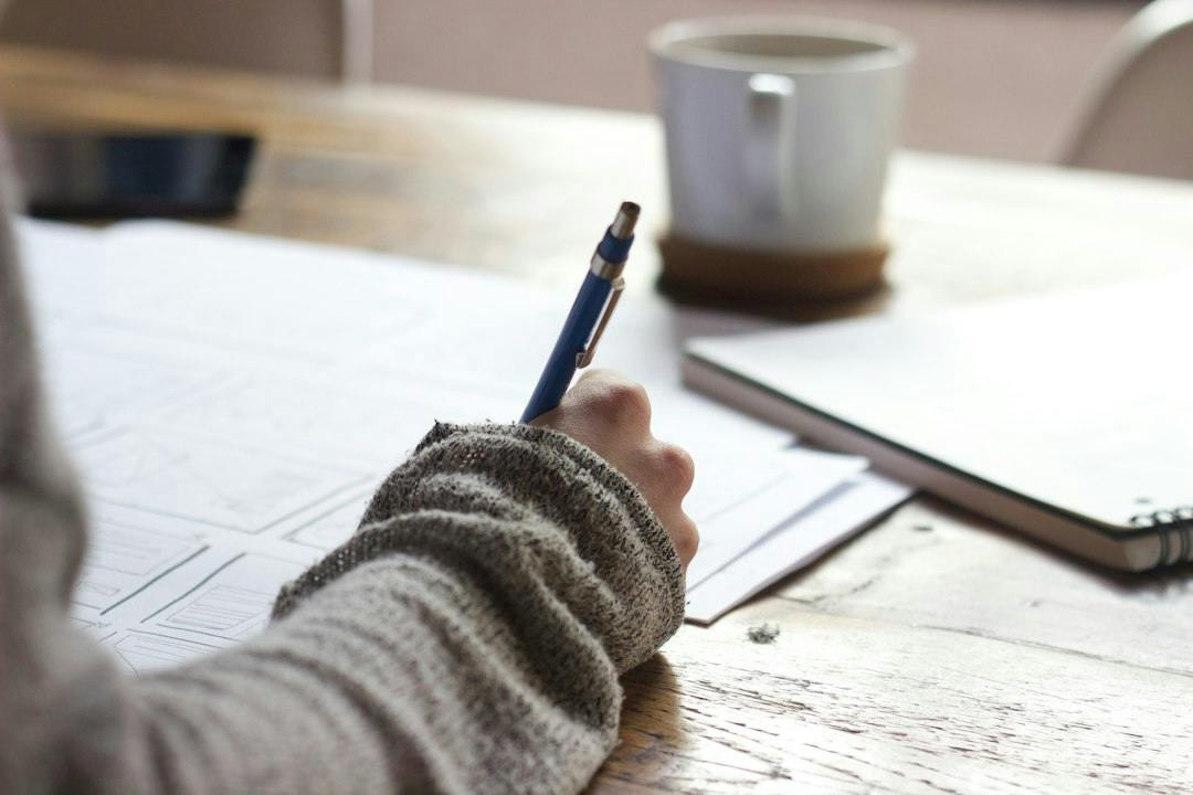 Person filling in a form at a wooden table next to a mug (Photo by Unseen Studio on Unsplash)