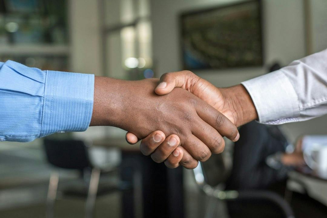 Two people shaking hands across a table (Photo by Cytonn Photography on Unsplash)