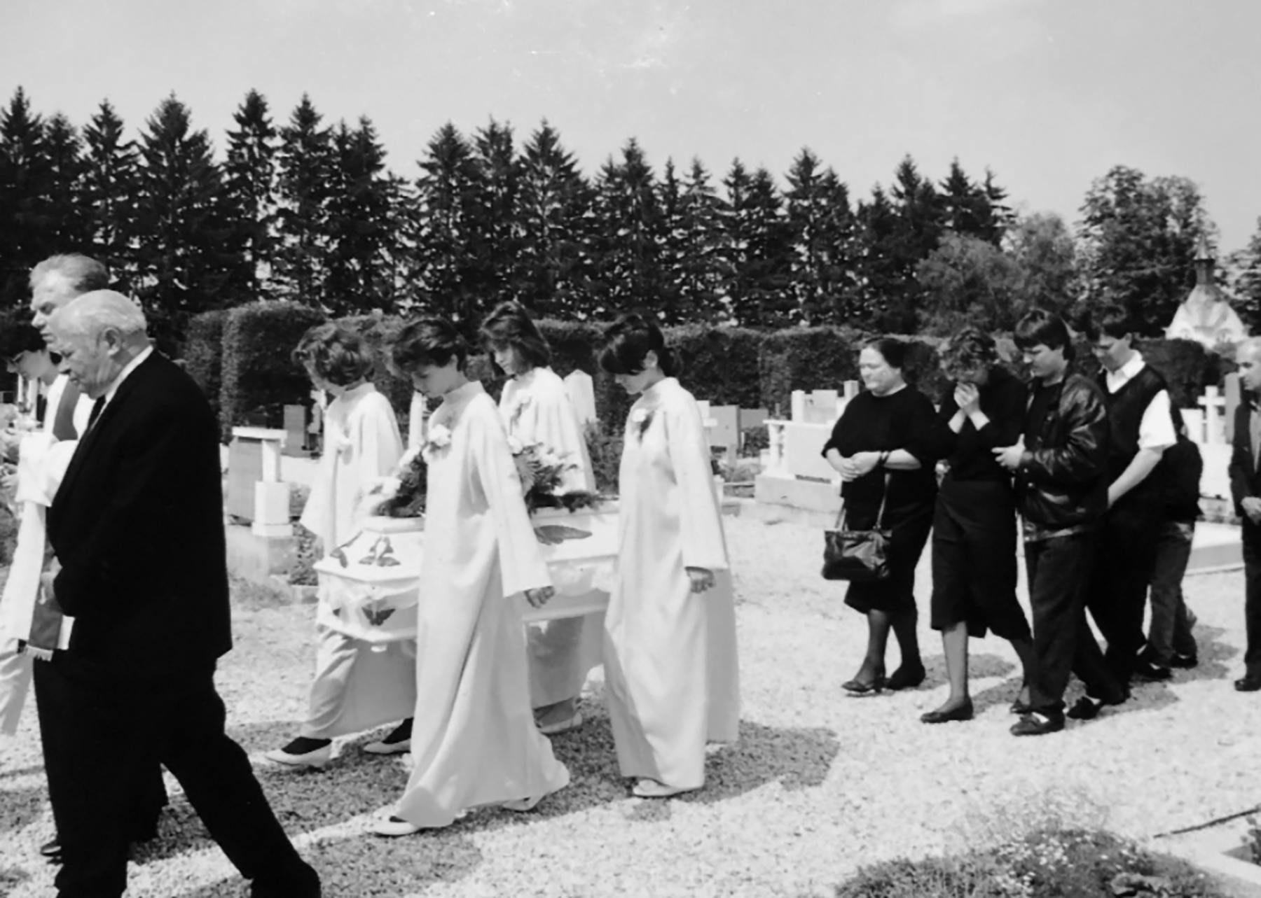 Črno-bela fotografija pogrebnega sprevoda, na njej štiri mlada dekleta v belem nosijo majhno belo krsto