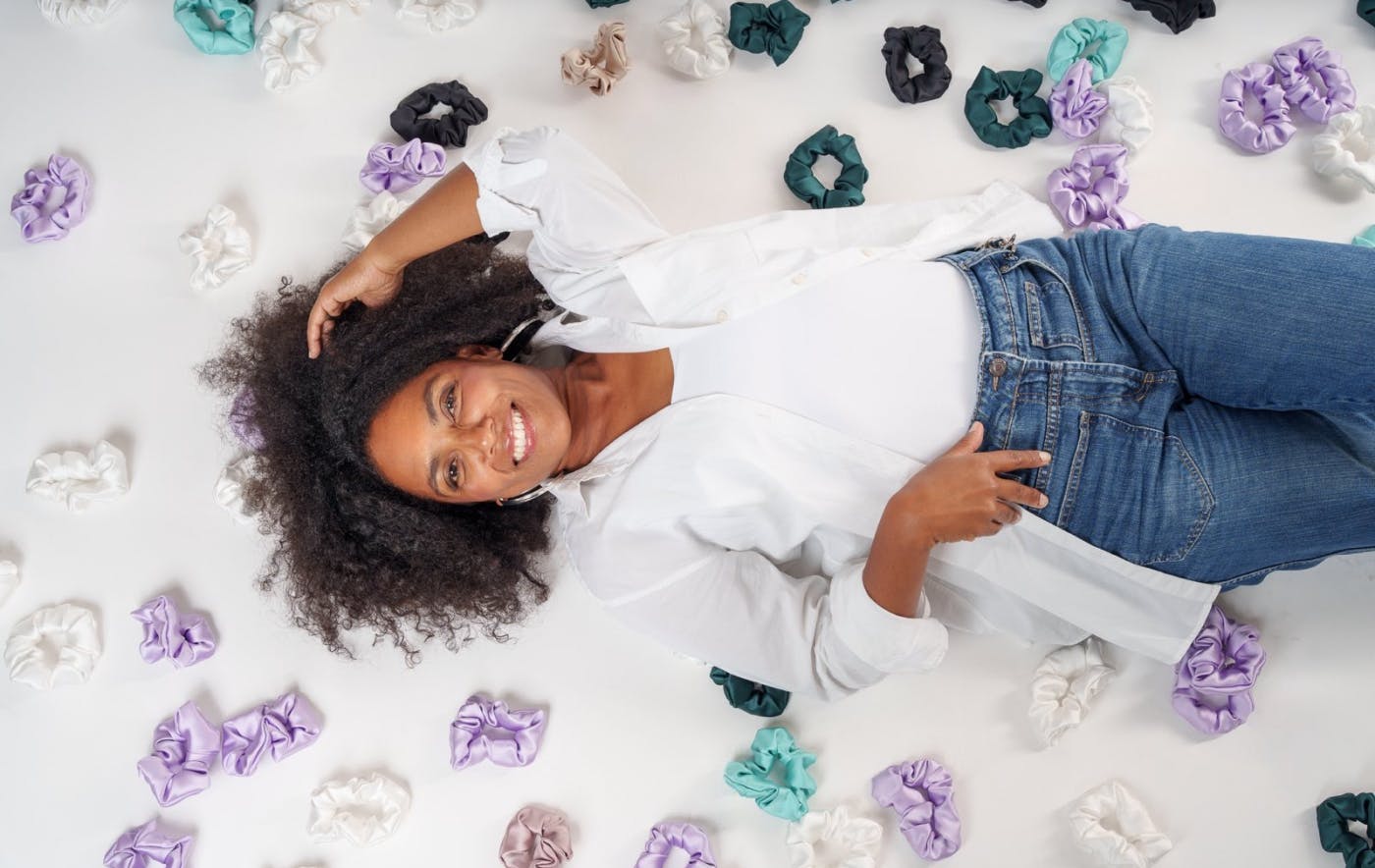 Portret intervjuvanke od zgoraj, ona leži na tleh, roko ima v laseh, okoli nje ležijo številne gumice za lase