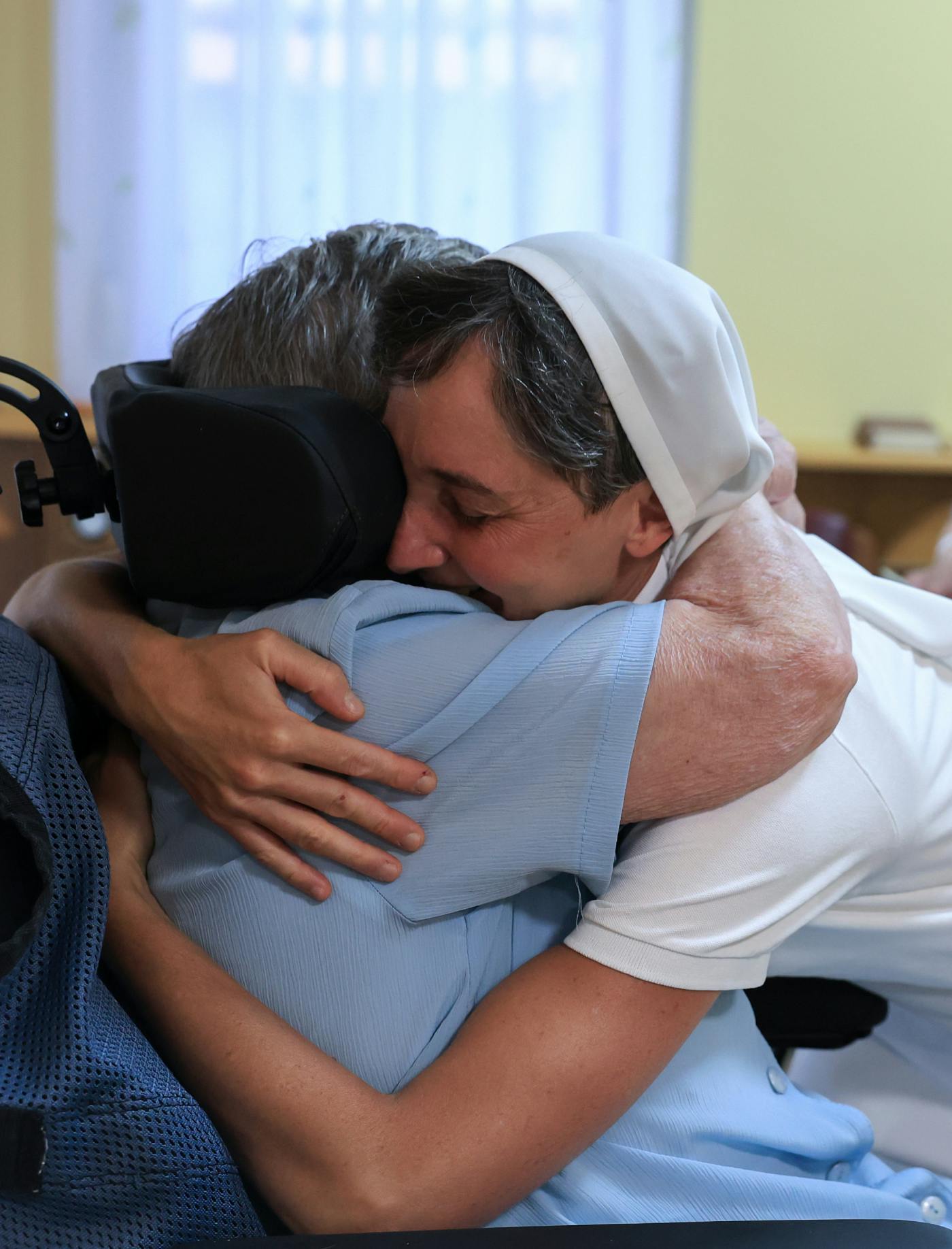 Redovnica in starejša ženska na invalidskem vozičku v objemu