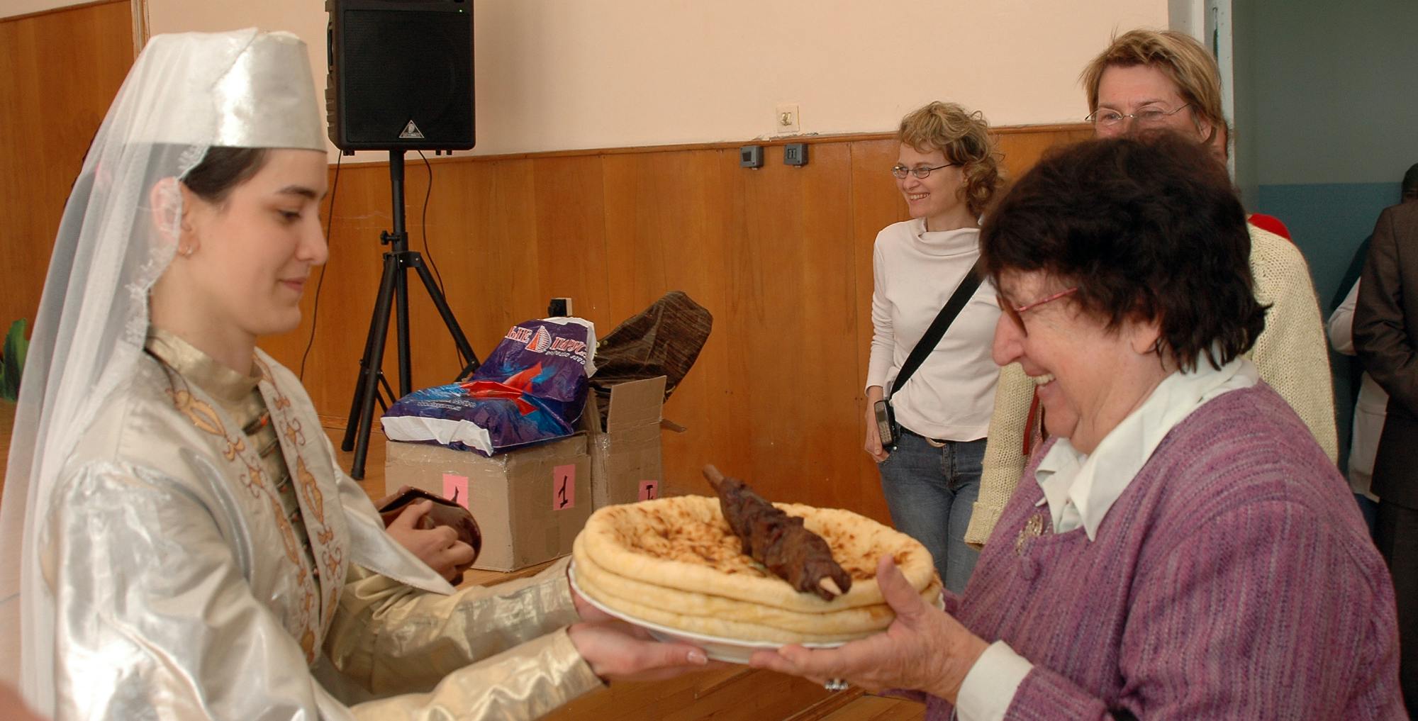 dr. Mikuš Kos od dekleta v noši sprejema hrano na krožniku