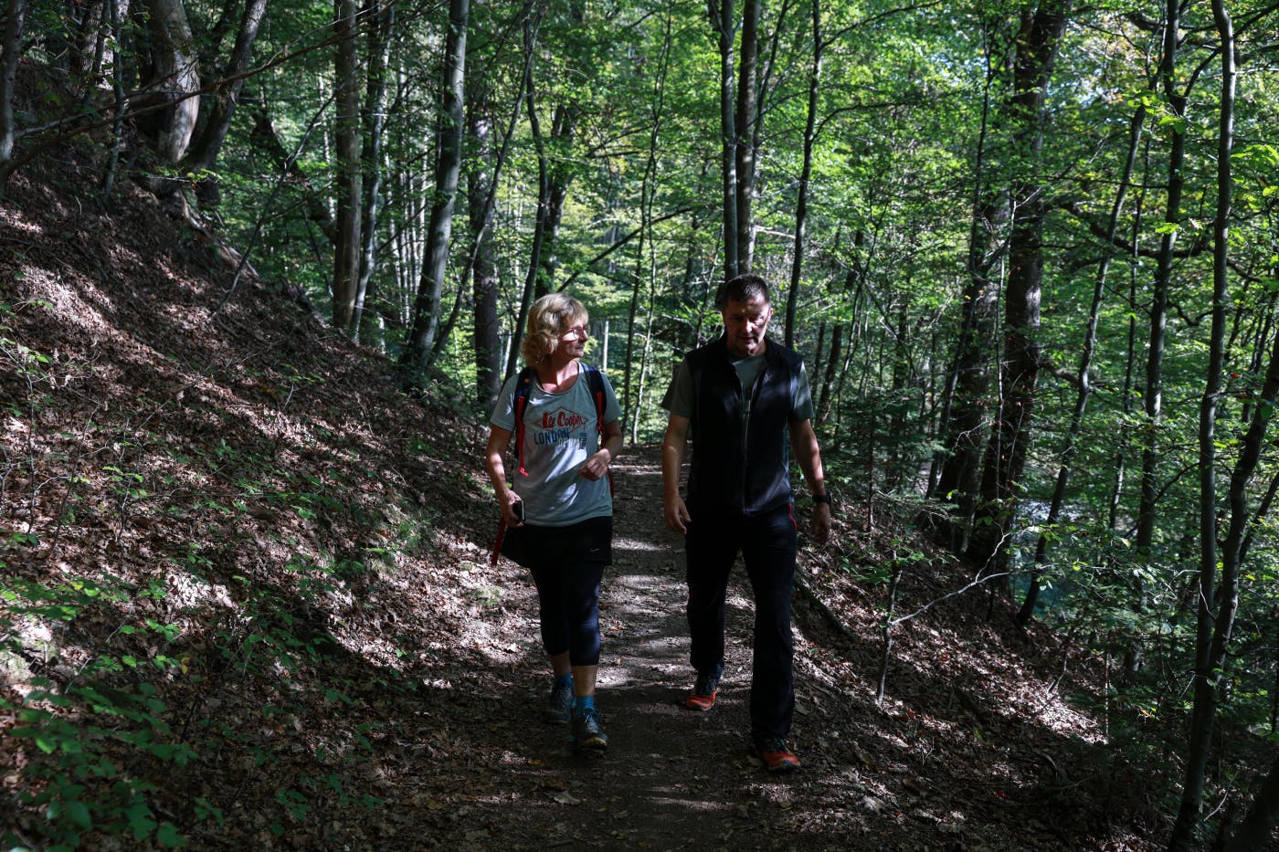 Ženska in moški v športnih oblačilih hodita po senčni gozdni poti