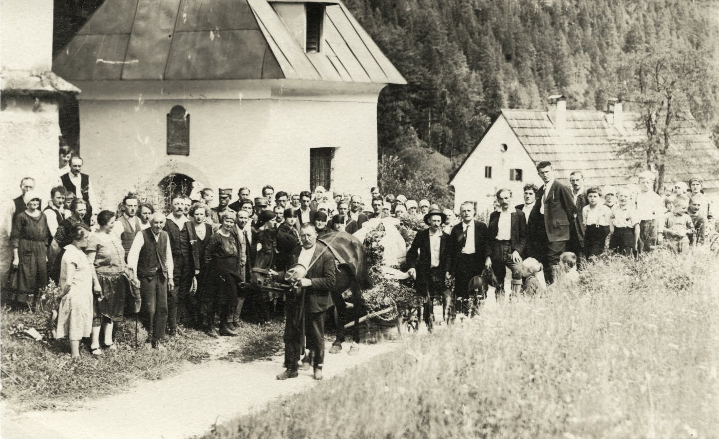 Starejša črno-bela fotografija velike skupine ljudi na vasi, gledajo v fotoaparat