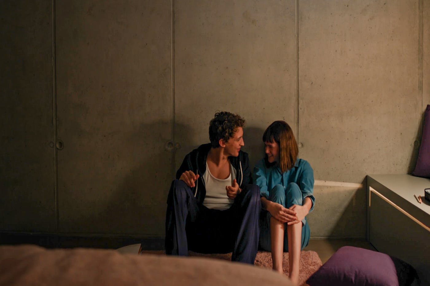 Kader iz filma, lika sedita skupaj na tleh spalnice in se smejita