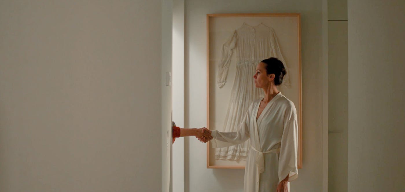 Kader iz filma, ženski like se rokuje z nekom, ki je skrit za vrati