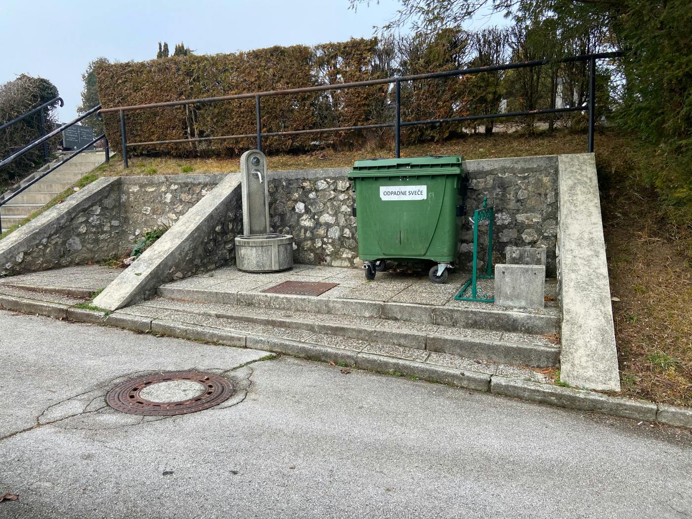 Prostor s kontejnerjem z napisom "odpadne sveče", zraven katerega je pipa
