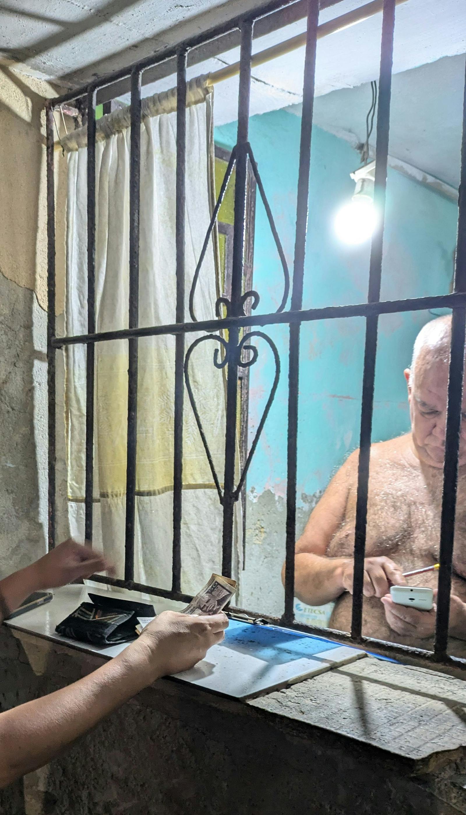 Moški brez majice, ki na oknu za rešetkami zamenjuje denar