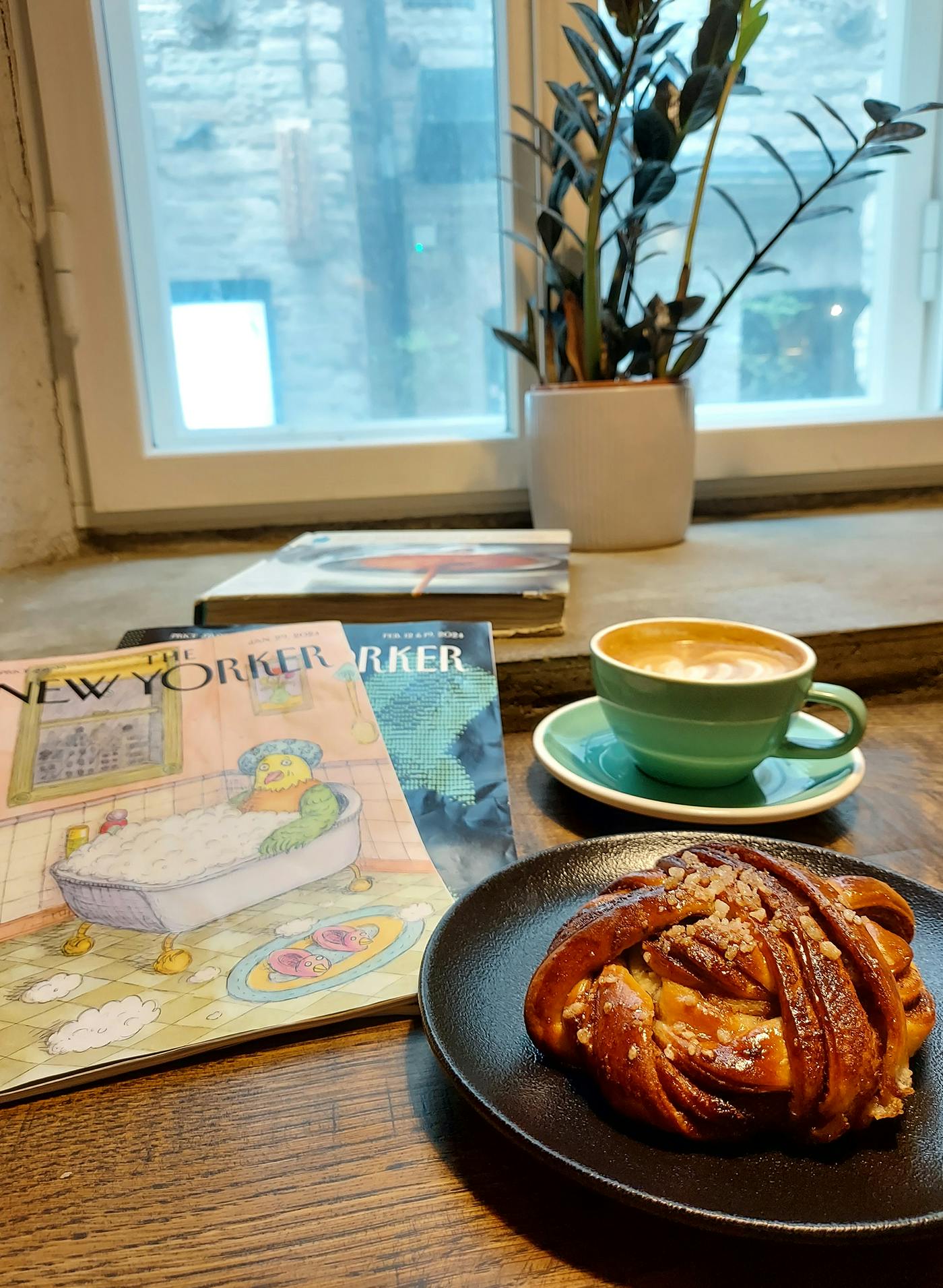 Miza v kavarni, na njej pecivo, kava in revije The New Yorker