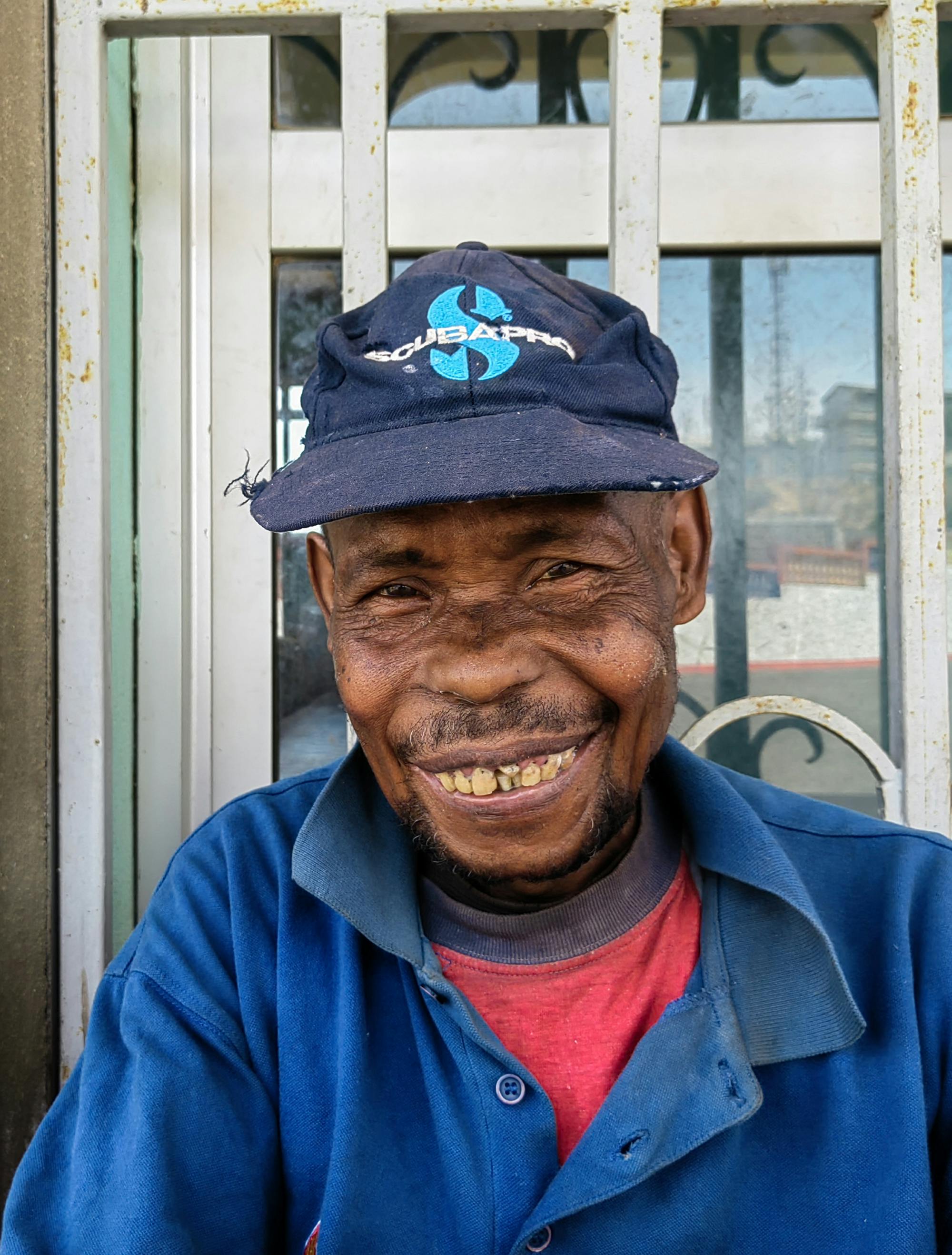 Portret nasmejanega moškega s krivimi zobmi in šilt kapo