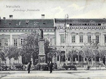 Stara razglednica. Trg s spomenikom, v ozadju pročelje stavb. Na enem od njih je napis Kazino. Črnobela reprodukcija.