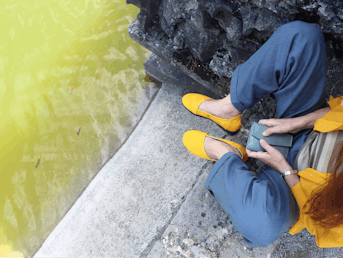 Ženska, fotografirana od zgoraj z rumenimi čevlji in srajco, sedi ob reki