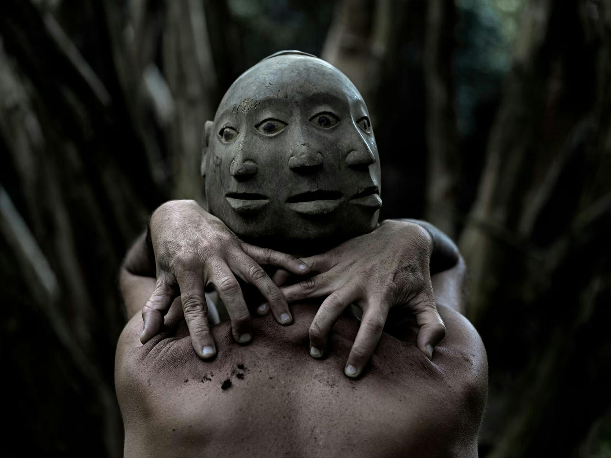 Človek, fotografiran od zadaj, na glavi ima masko s tremi prepletenimi obrazi