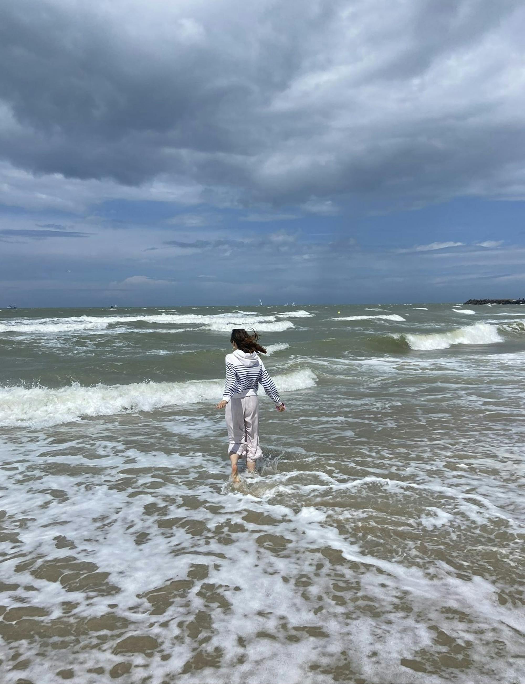 Avtorica prispevka namaka noge v razburkanem morju, nad njim so nevihtni oblaki