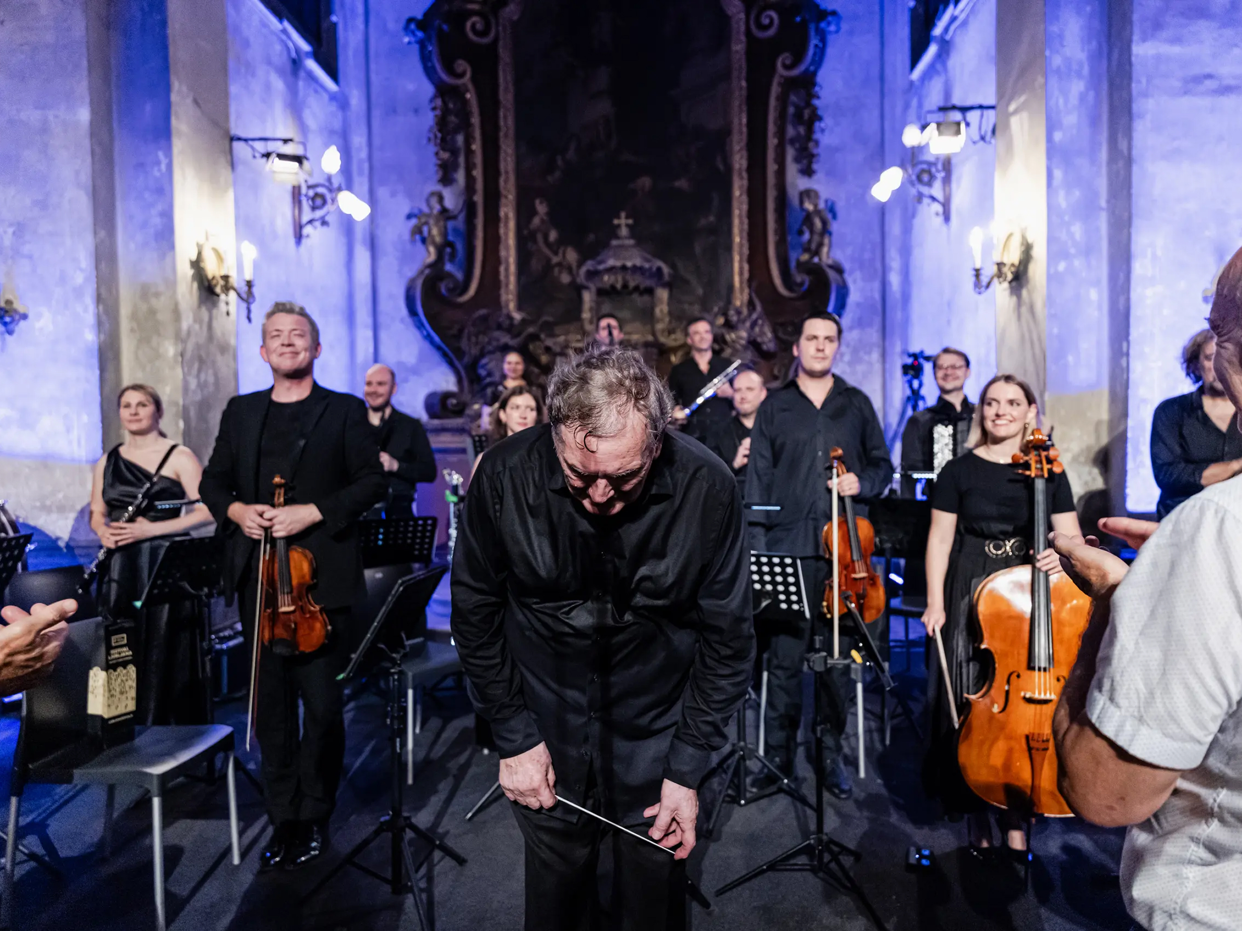 Dirigent v priklonu, za njim je orkester