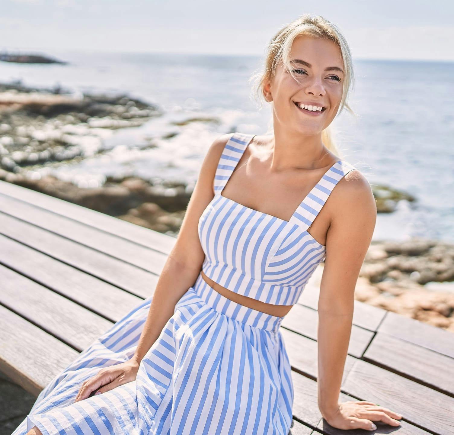 Woman smiling in dress sitting on bench on the beach