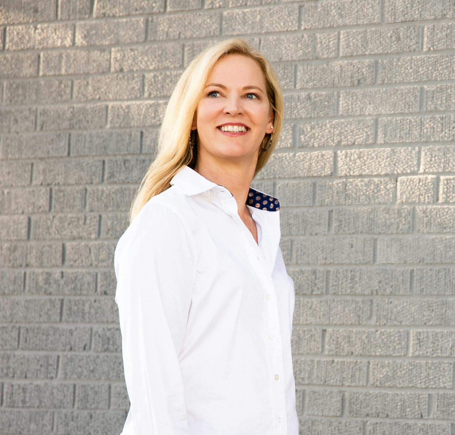 Woman smiling and looking to her right standing next to brick wall