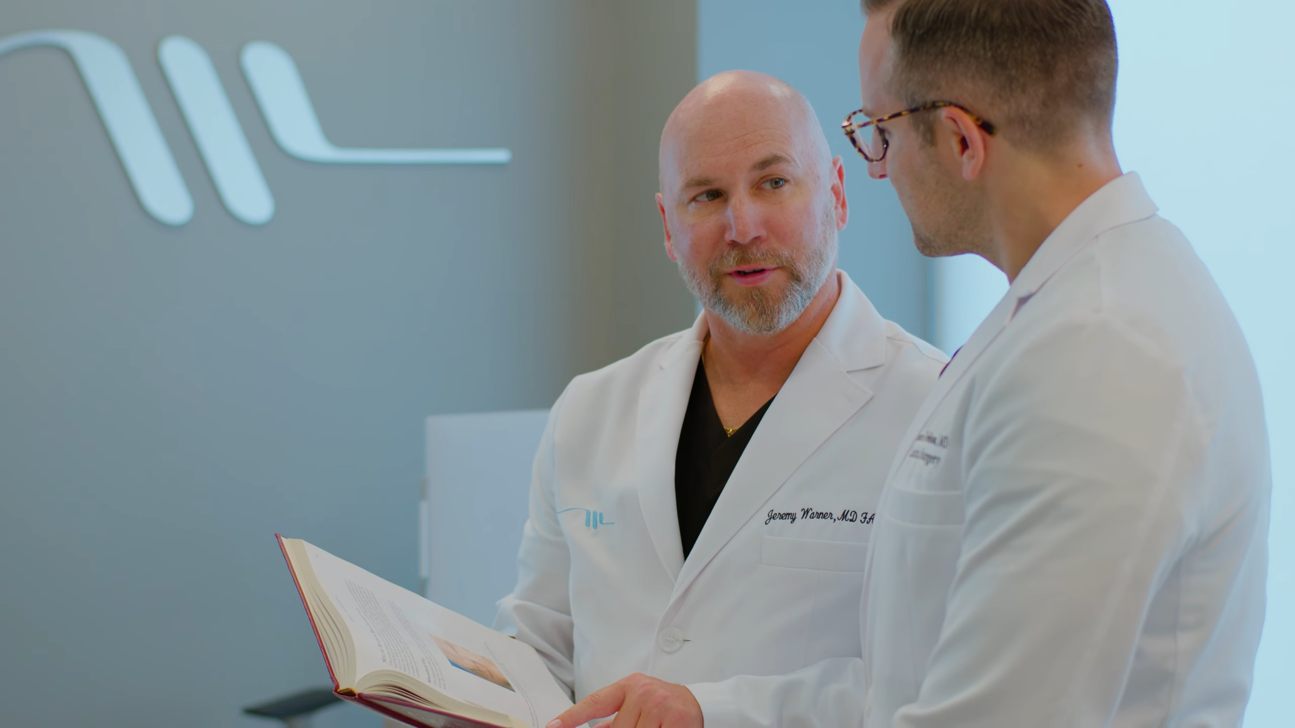 Dr. Warner teaching another doctor and holding book