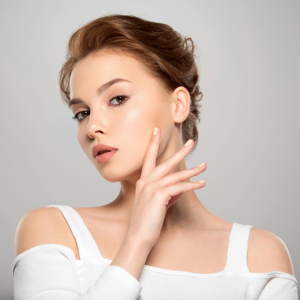 Model wearing white blouse touching her face
