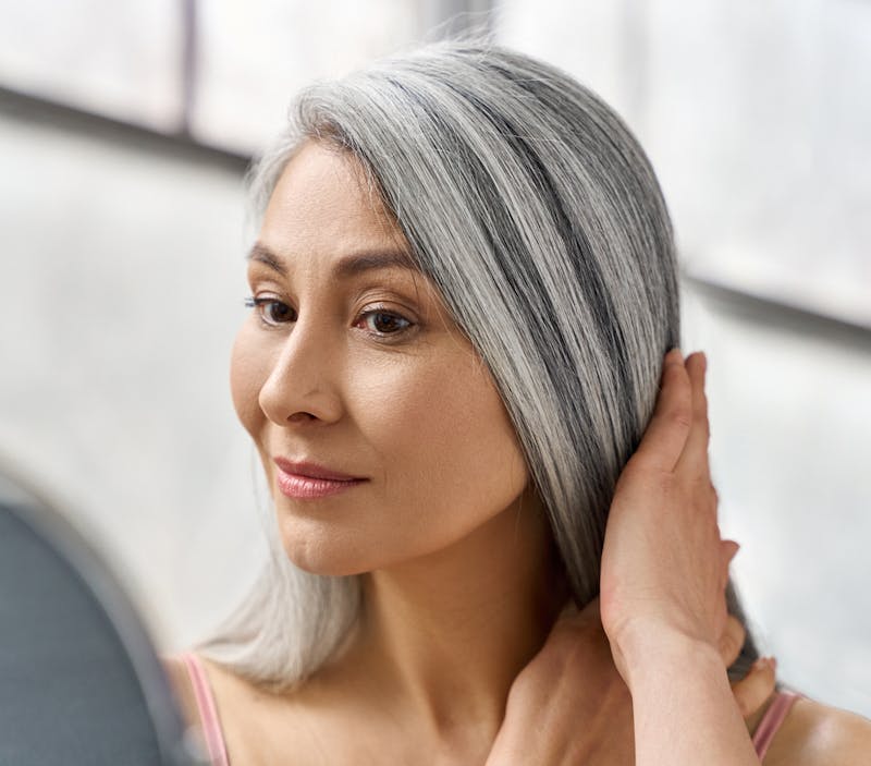 woman with grey hair looking at the mirror