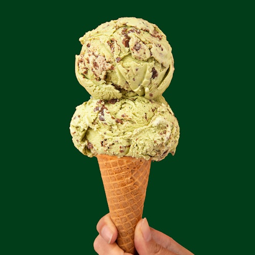 double scoop of molly moon's matcha chip ice cream in a sugar cone on a dark green background