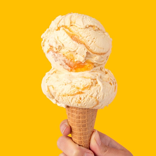 double scoop of molly moon's triple citrus ice cream in a sugar cone on a lemon yellow background
