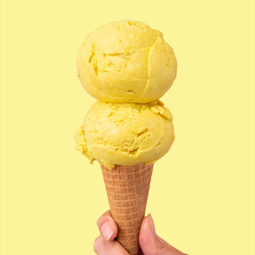 double scoop of molly moon's vegan golden milk ice cream in a sugar cone on a light yellow background