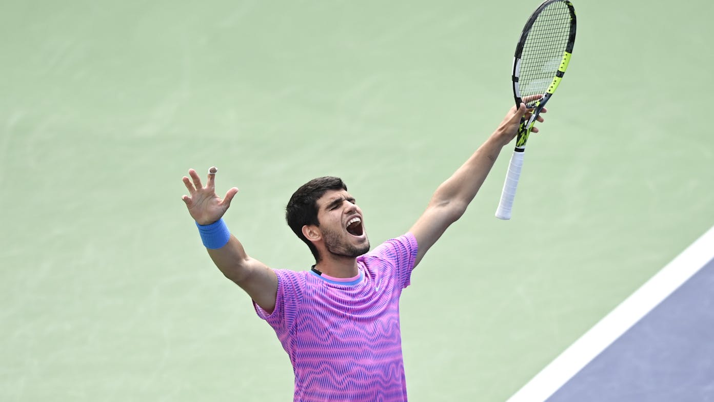 Carlos Alcaraz raises his arms and racket in celebration of his 2024 BNP Paribas Open champion victory.