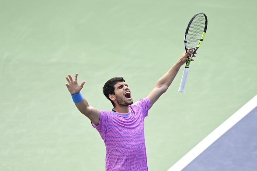 Carlos Alcaraz raises his arms and racket in celebration of his 2024 BNP Paribas Open champion victory.