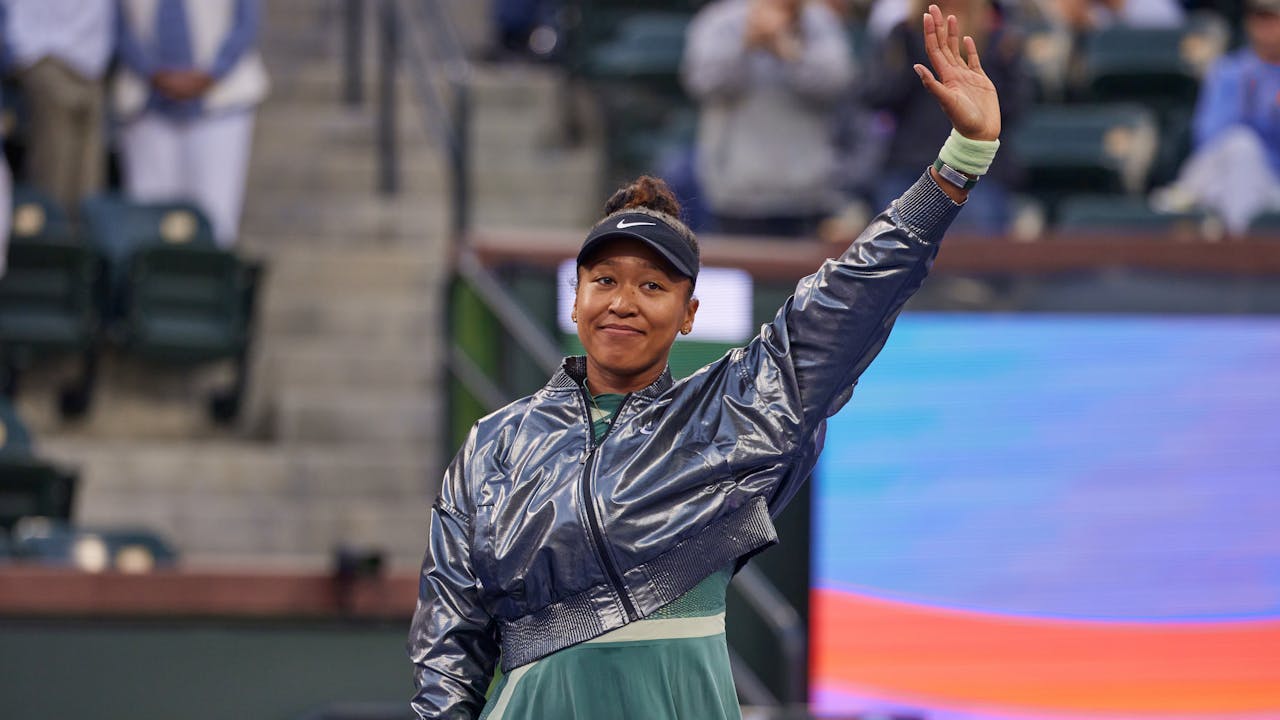 Naomi Osaka raises her hand on the court to thank her fans.