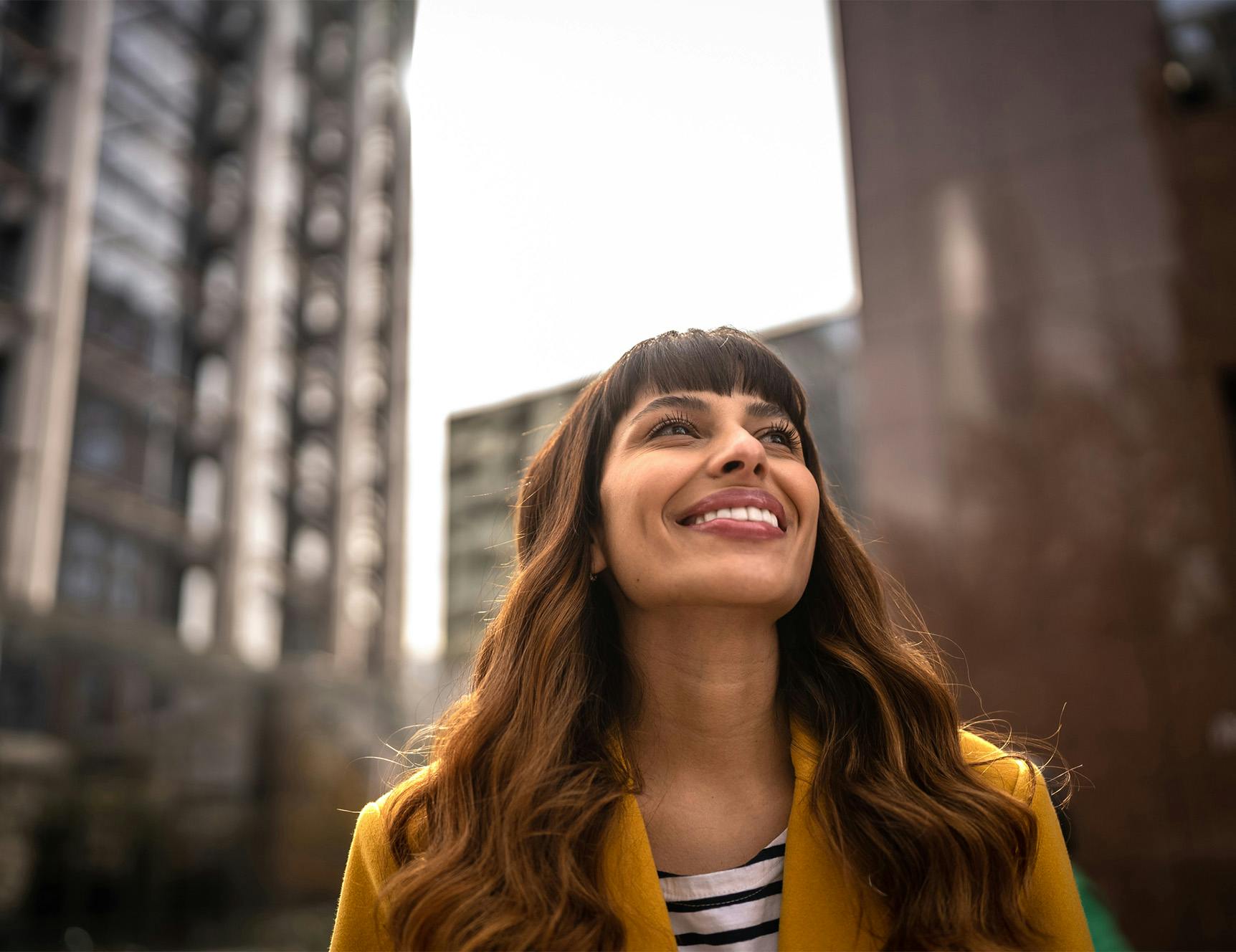 woman smiling and looking up at tall buildings