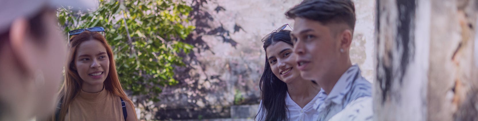 Young adults in conversation outdoors, smiling and engaged, with greenery and a stone wall in the background.