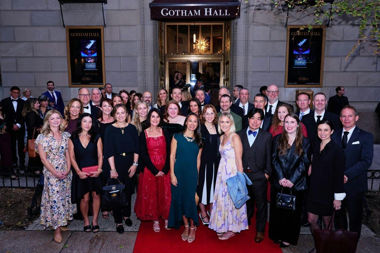 Group of Inizio colleagues dressed in formal attire posing together on the red carpet outside Gotham Hall in New York City.