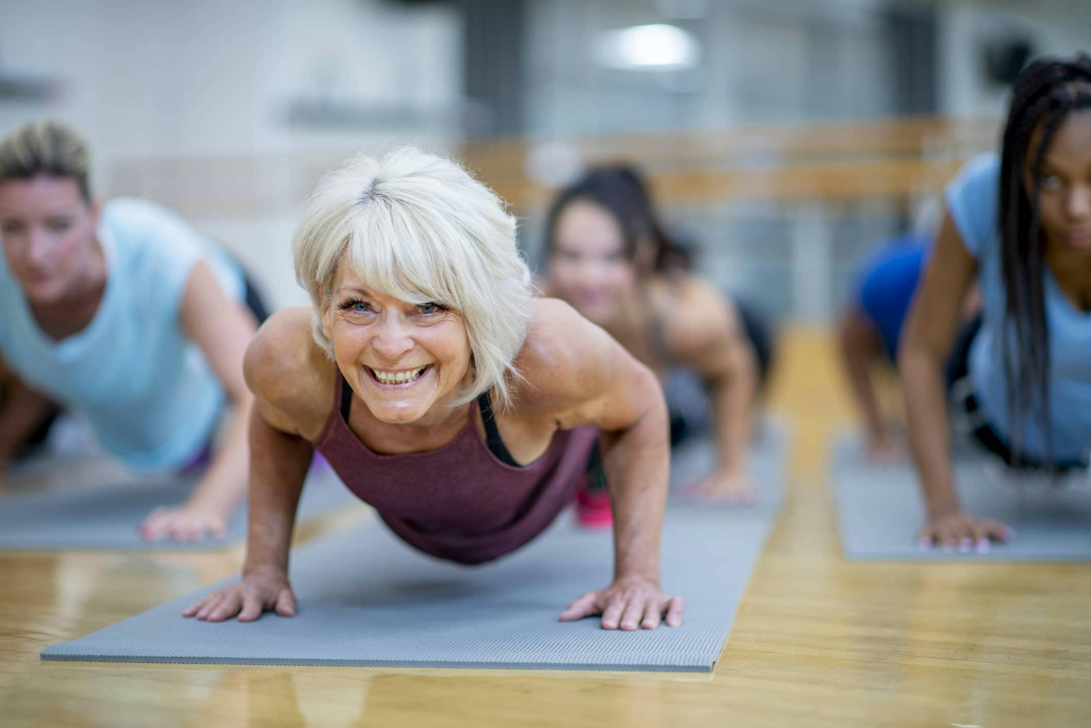 older woman smiling and doing yoga with group of young adults