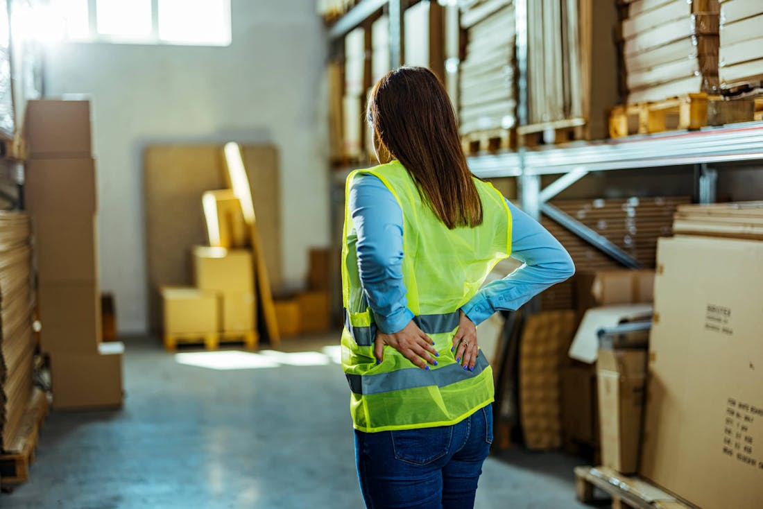 woman holding lower back at warehouse